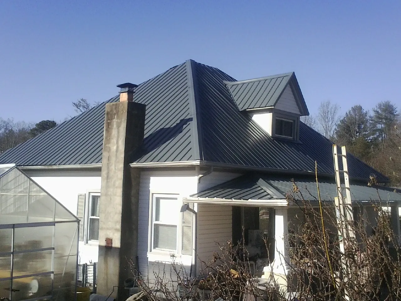 Dark blue standing seam metal roof on a white farmhouse with dormer — Slate & Tile Roof Repair by Roofing Brothers in South Fork