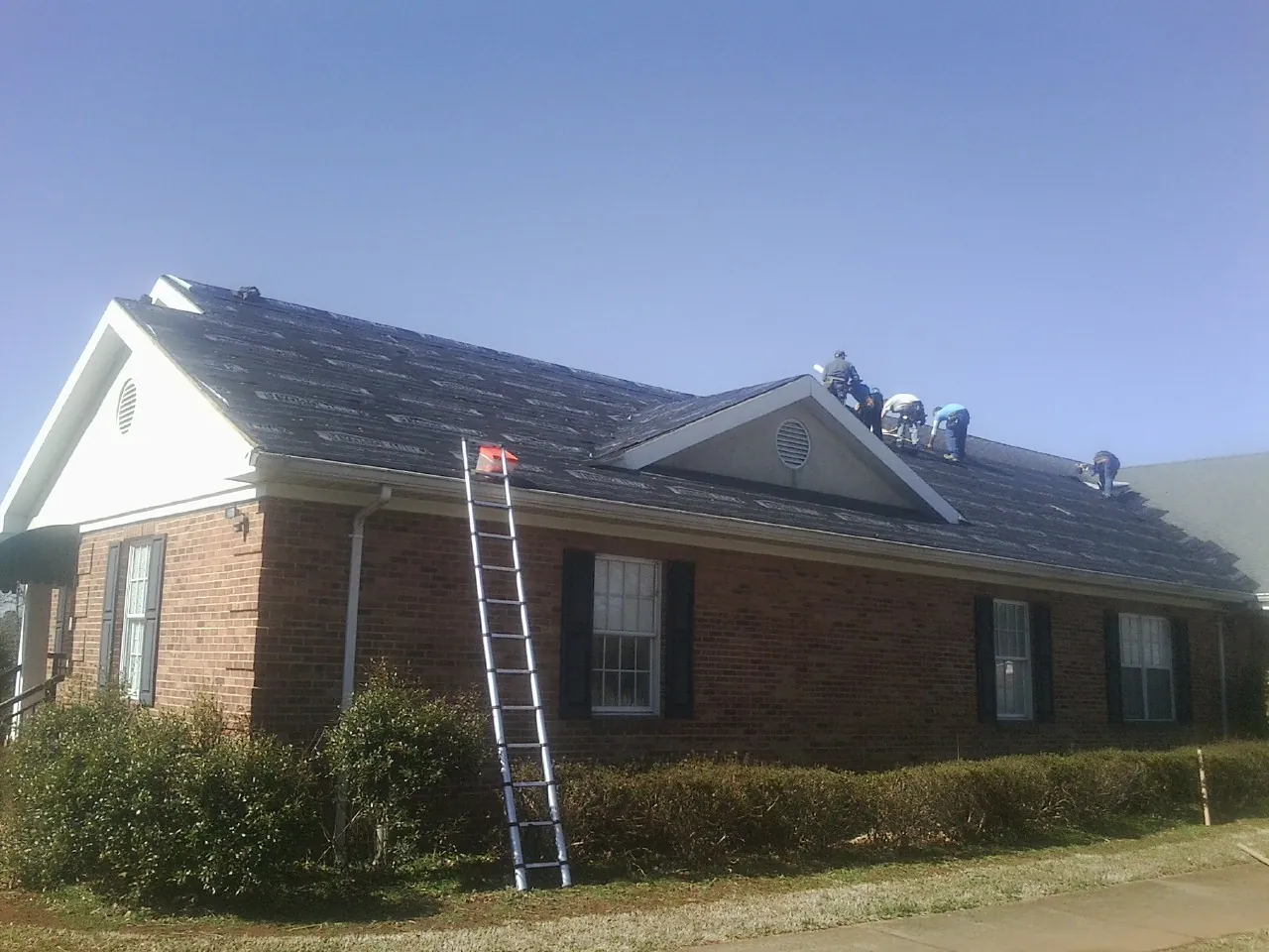 Crew tearing shingles off a brick ranch roof with a ladder set — Metal Roof Repair work by our crew in South Fork