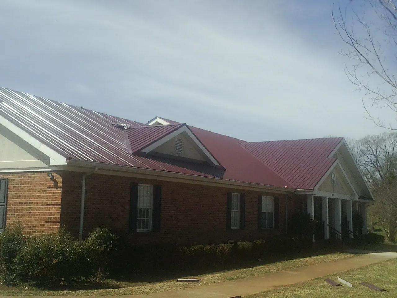 Red metal roof with gabled entries on a long brick building, from a Hail Damage Roof Repair job in South Fork
