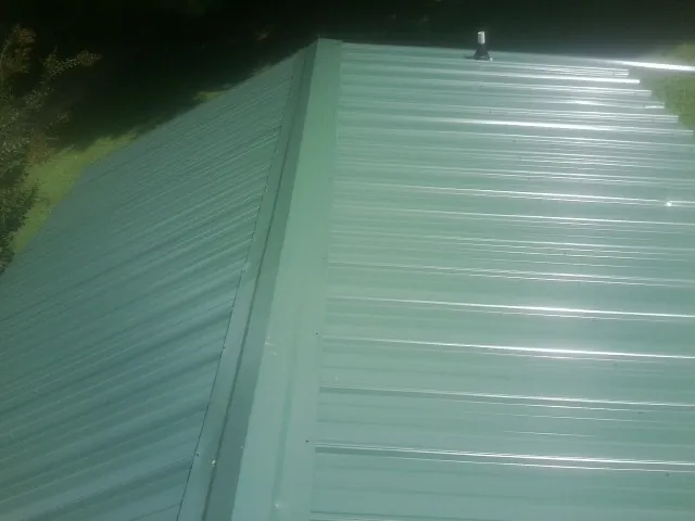 New green metal panels meeting at the ridge of a roof — Flat Roof Repair work by our crew in South Fork