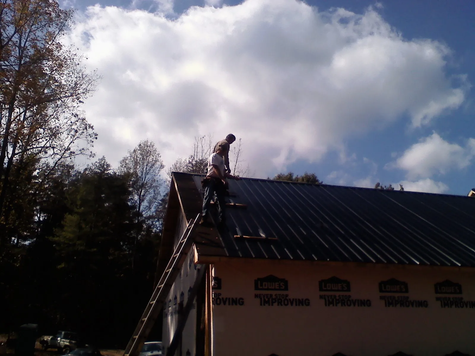Roofer fastening dark metal panels high against a cloudy sky, from a Roof Inspection job in South Fork