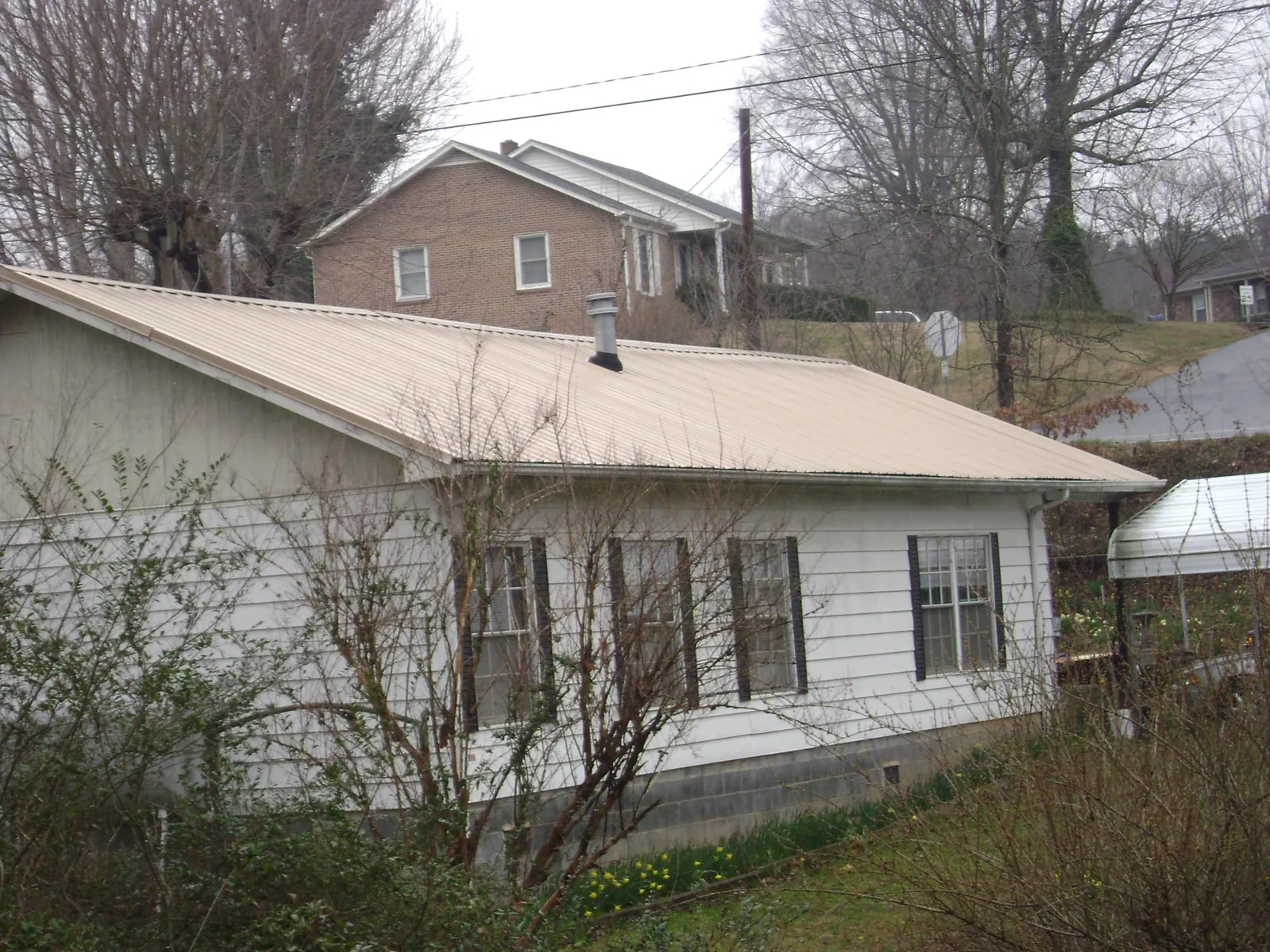 Tan metal roof on a white sided house set into a hillside — Commercial Roofing by Roofing Brothers in South Fork