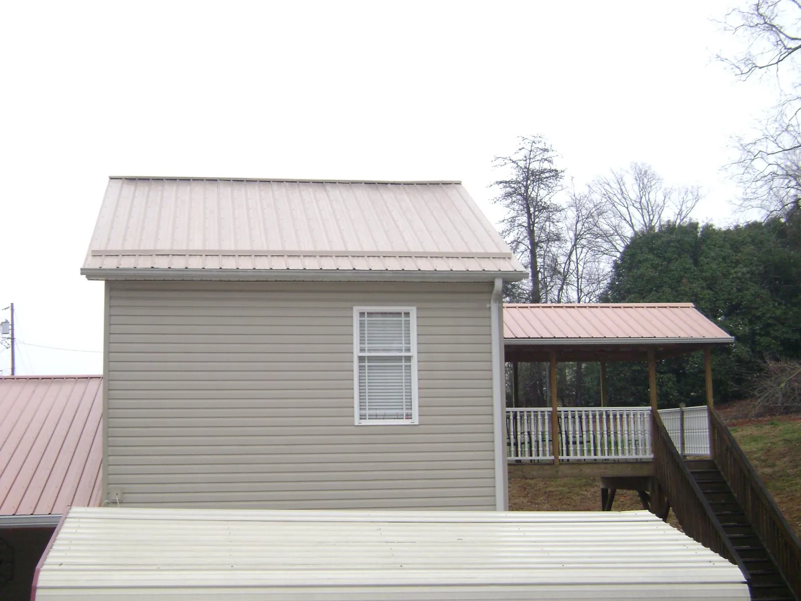 Tan metal roofs on a two story addition and attached porch, from a Roof Replacement job in South Fork